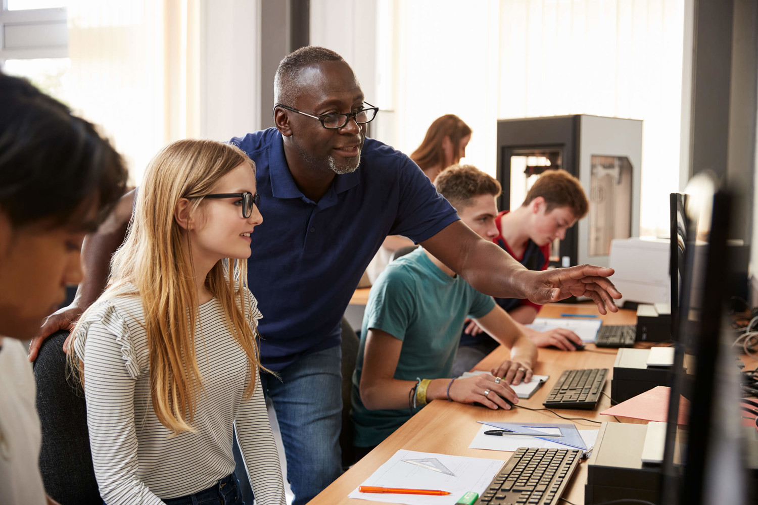 A teacher smiling with a female student on computer