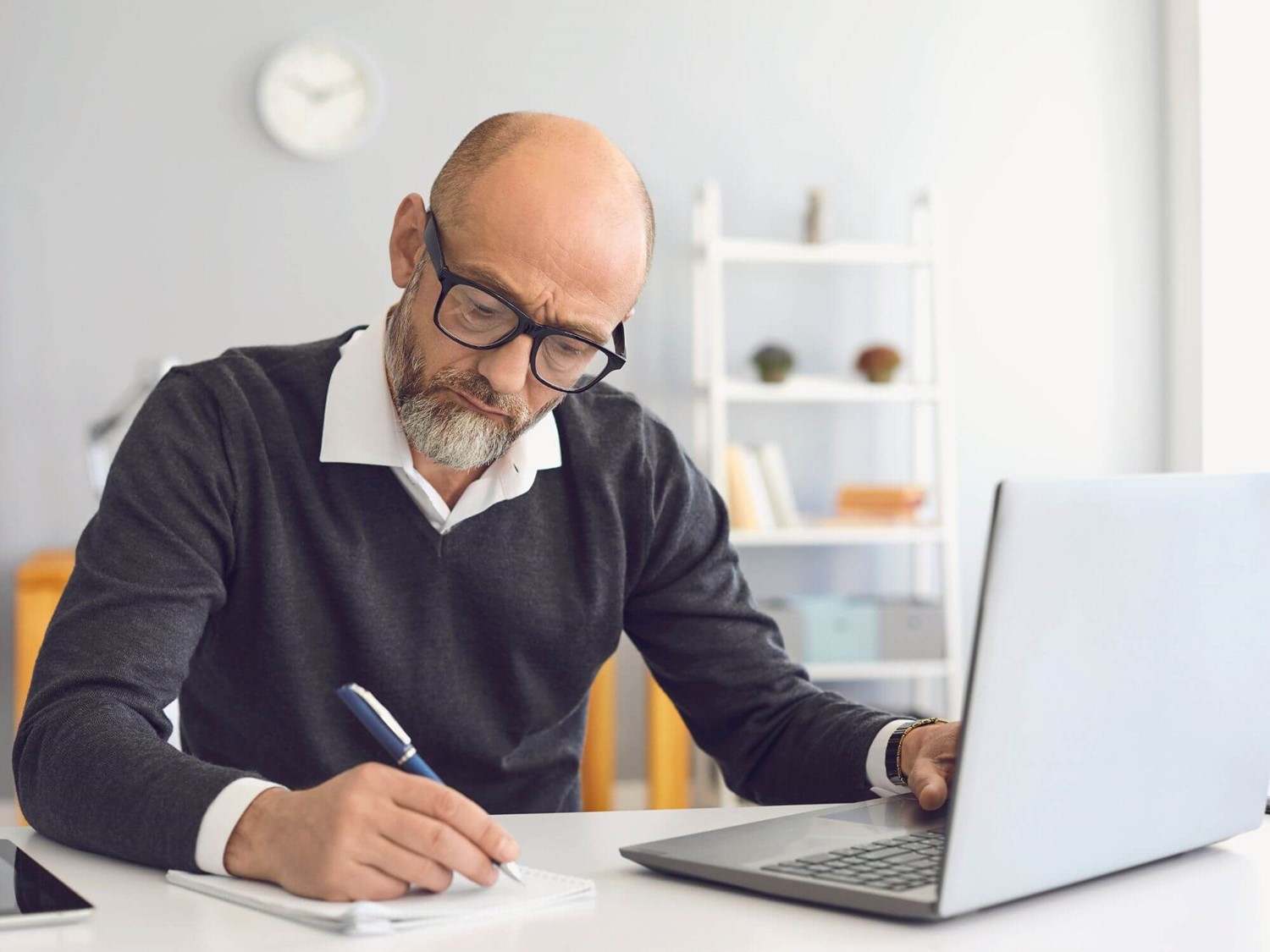 Man writing on notebook at laptop