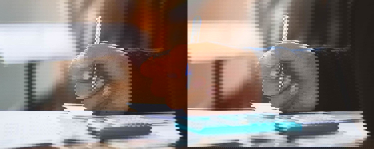 Close up of person holding pen with calculator on desk