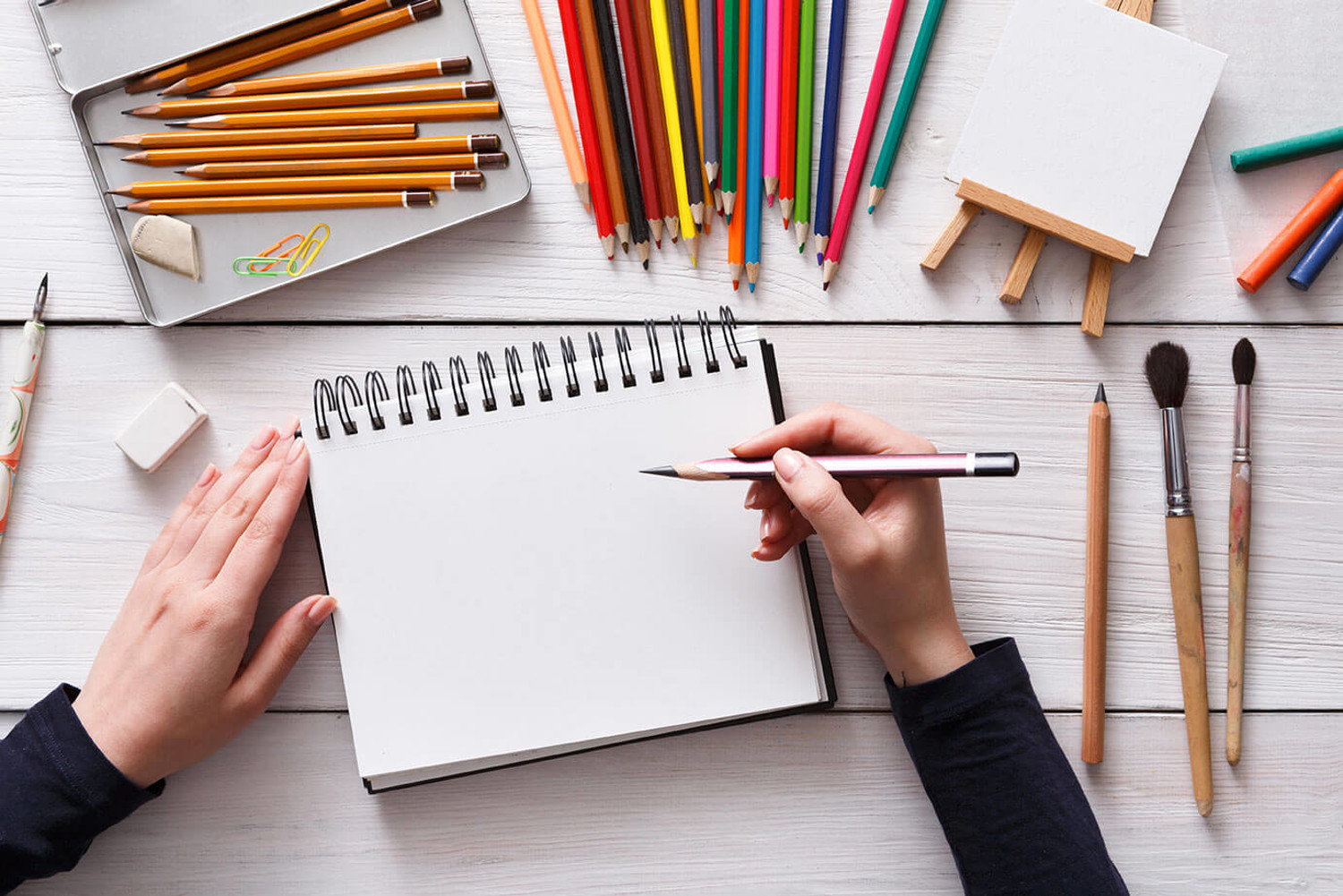 An artist starting to sketch on plain paper, surrounded by art tools and pencils.