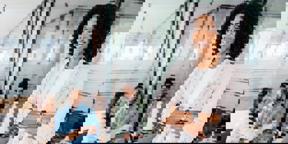 Smiling person looking at the camera with group of people sitting at a desk in the background