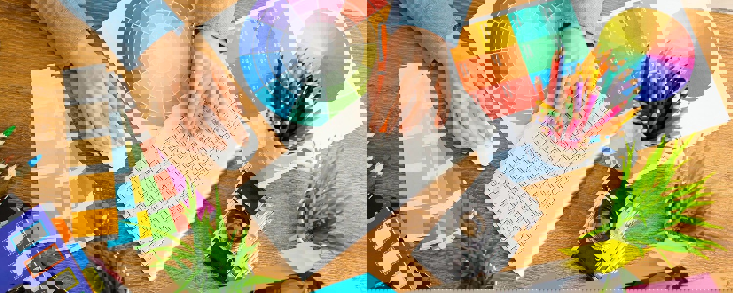Person's hands typing on keyboard with camera and colour charts on desk