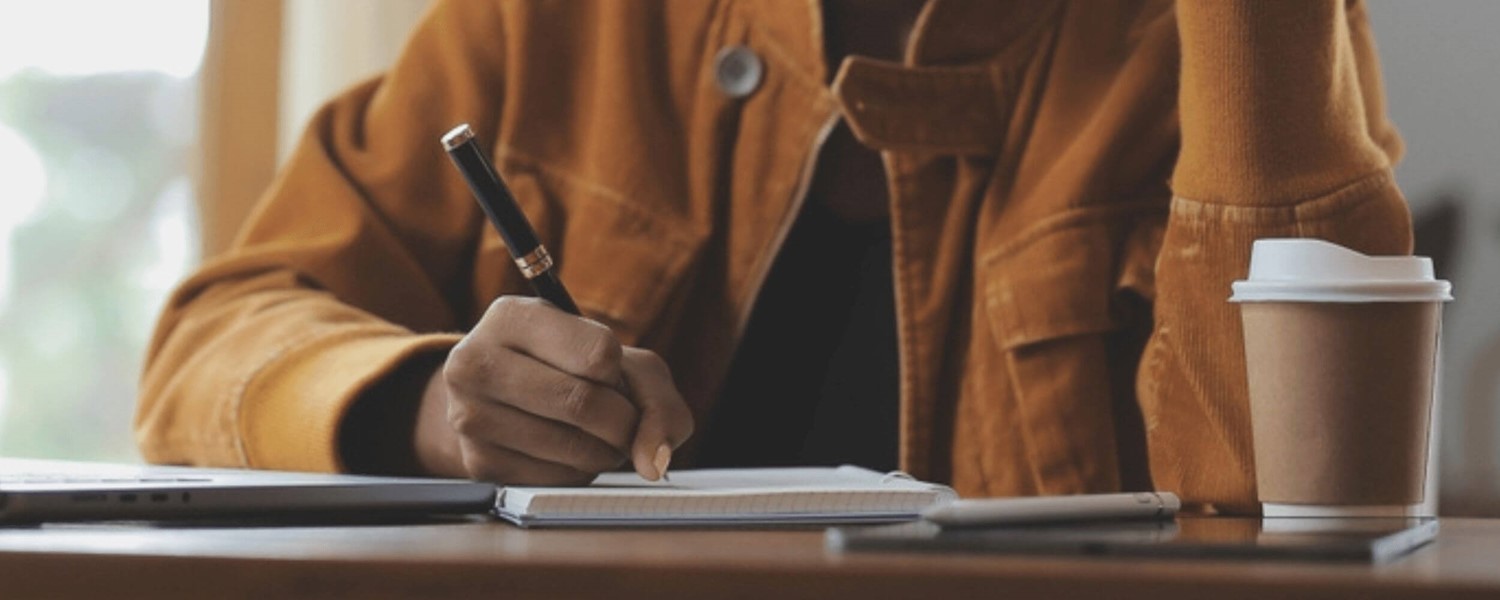 Person writing in notebook with coffee cup on desk