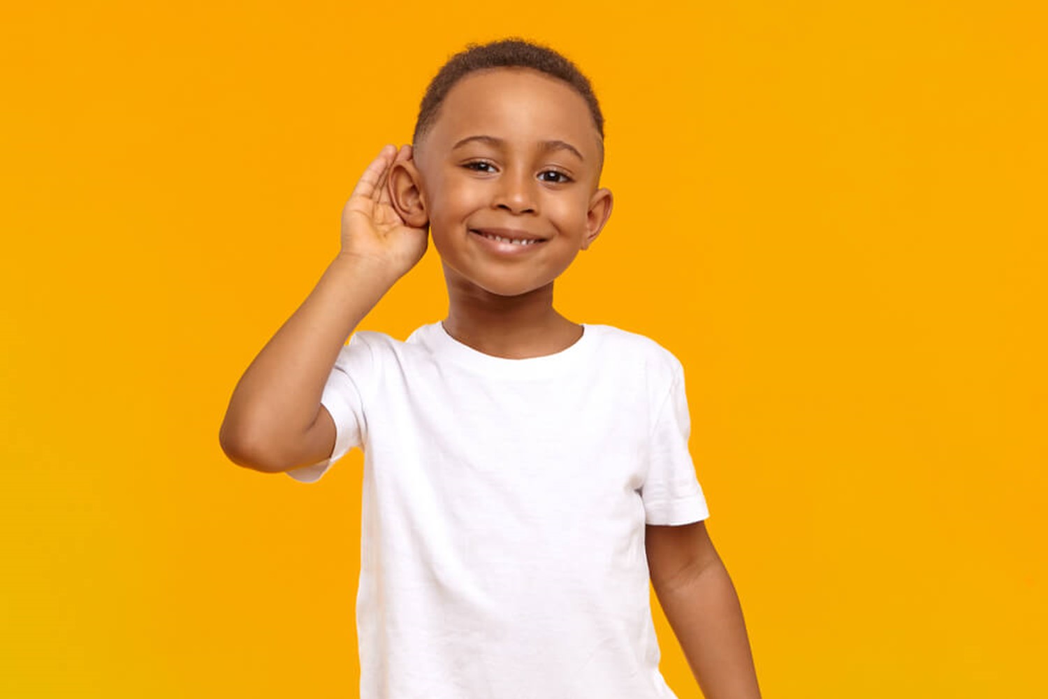 Smiling boy holding ear to listen