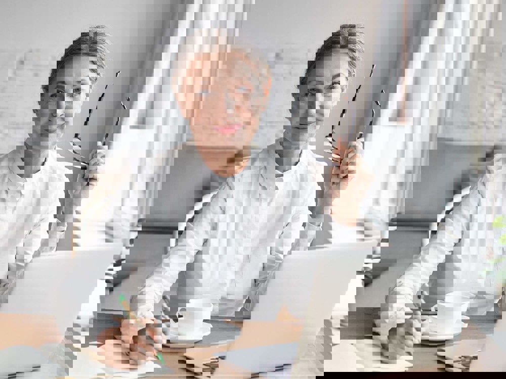 Lady writing in notebook at laptop