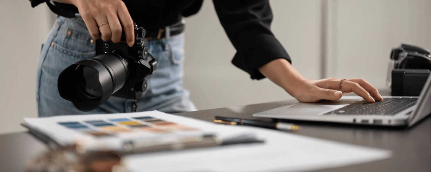 Close up of lady holding camera and typing on laptop