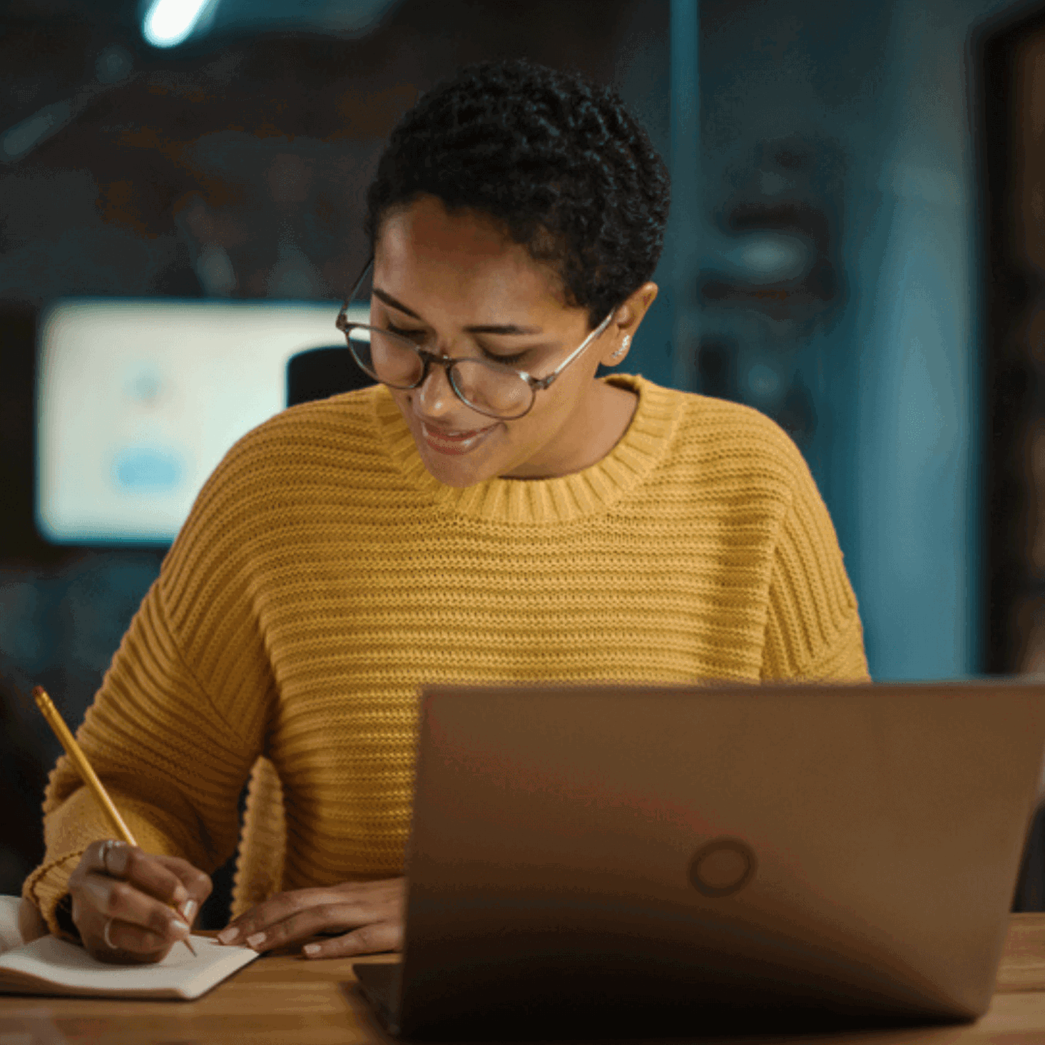 Lady writing in notebook at laptop