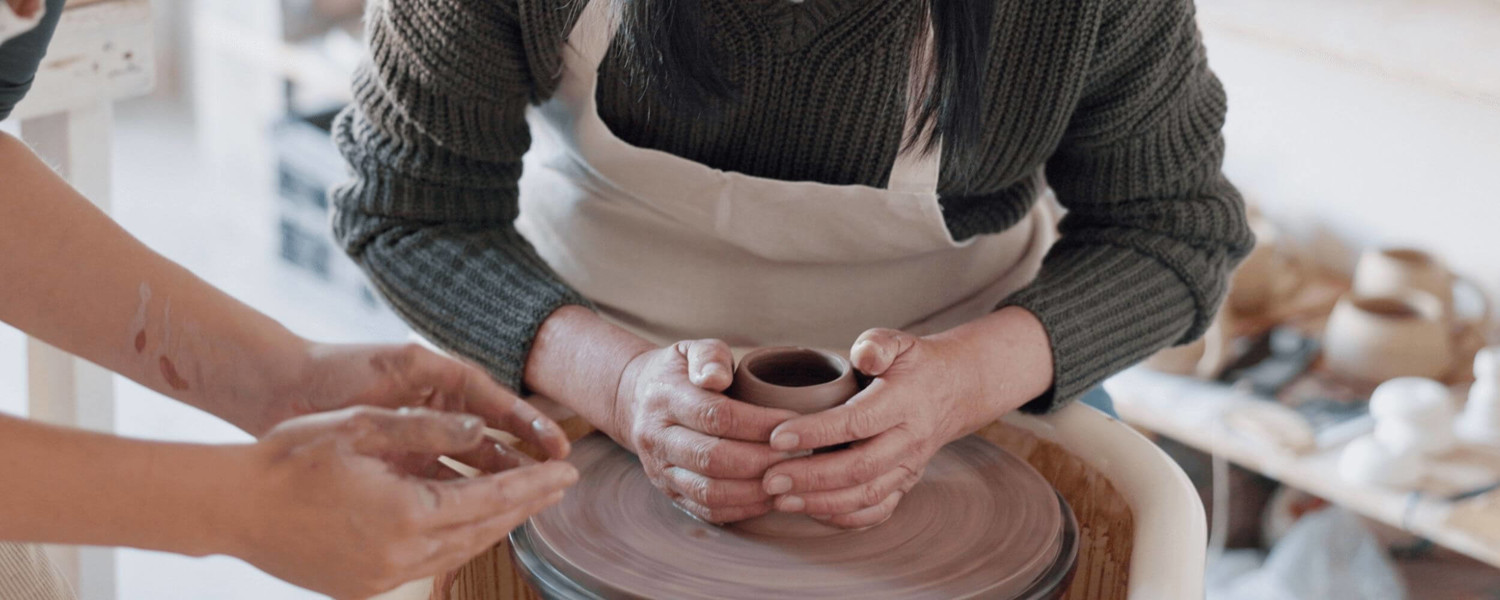 Close up of two people turning clay on pottery wheel
