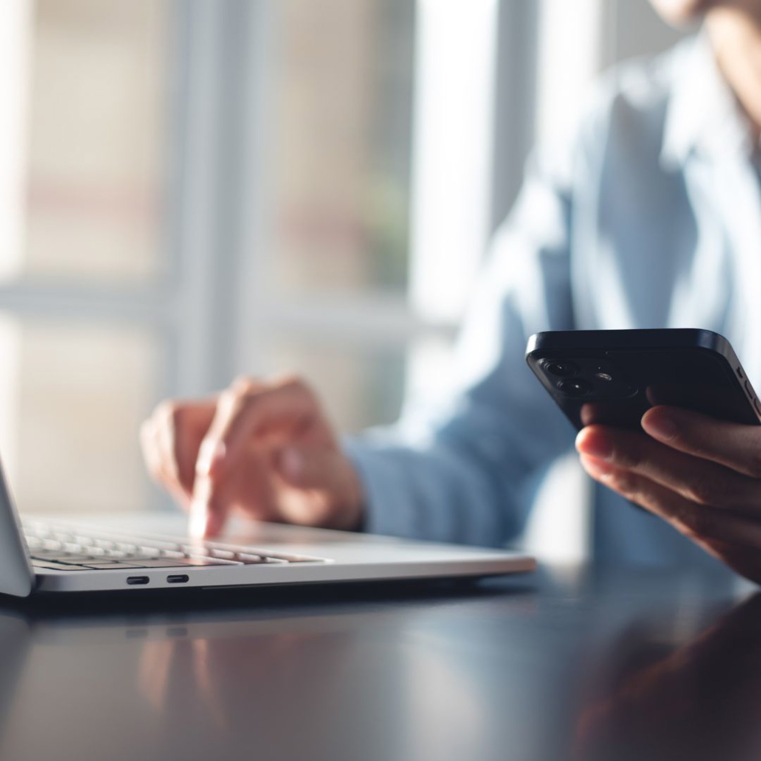 A person holding a phone and typing on a laptop