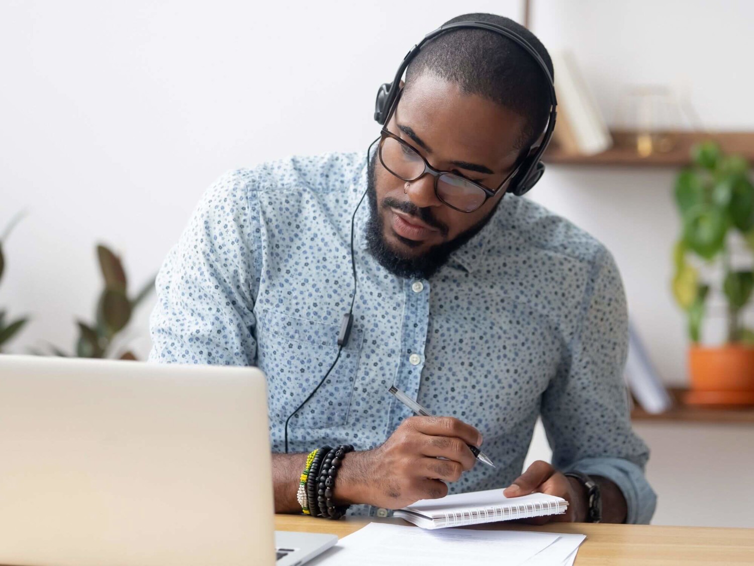 Man at laptop writing in notebook