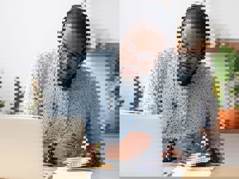 Man at laptop writing in notebook